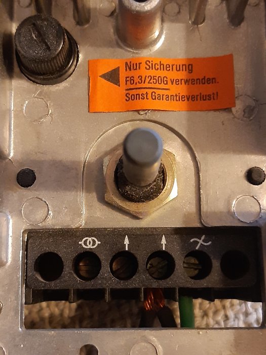 Elektrisk panel med varningsetikett, säkringhållare och koppartråd synlig i hål.