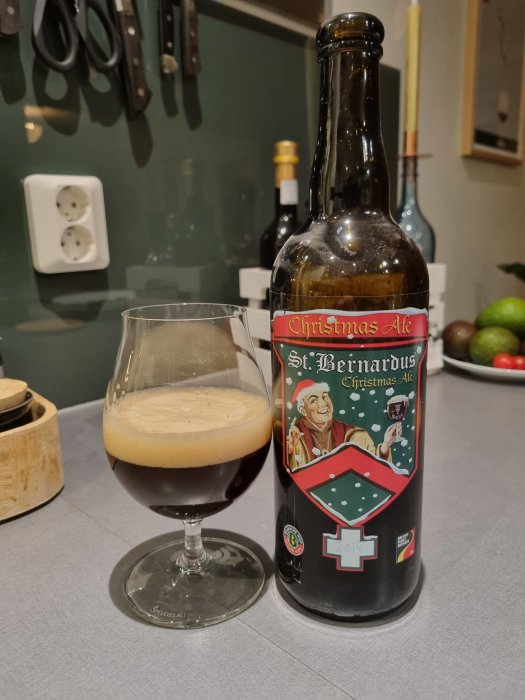 Ölflaska med etikett "Christmas Ale", mörkt öl i glas, köksmiljö i bakgrunden.
