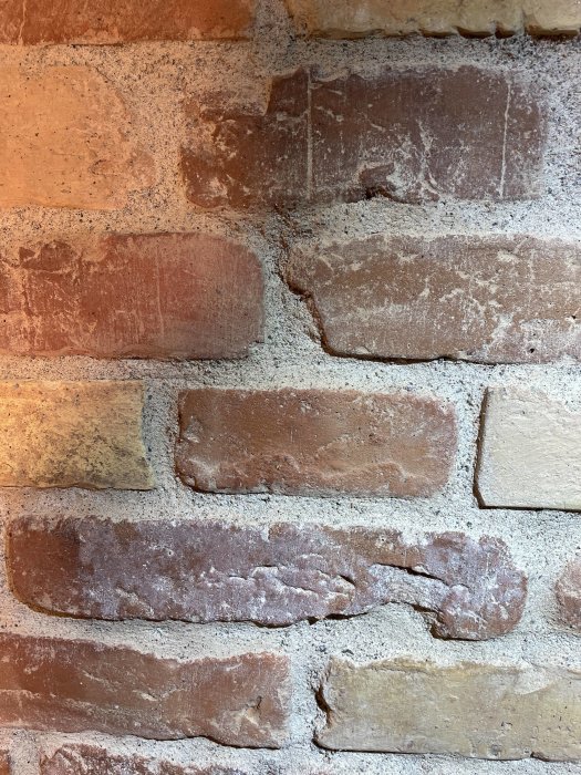 En närbild på en rödaktig tegelvägg med ojämn murbruk och varierande färgnyanser.