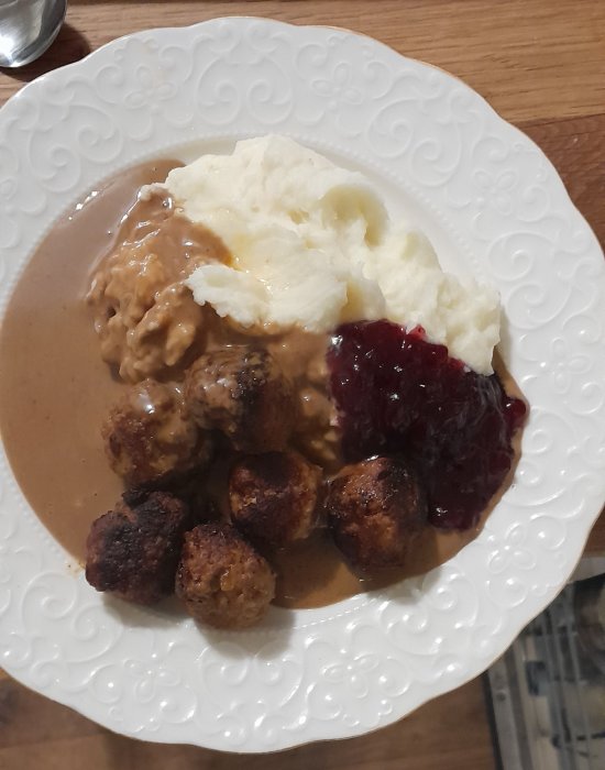 Köttbullar, potatismos, brunsås och lingonsylt på vit tallrik. Klassisk svensk måltid.