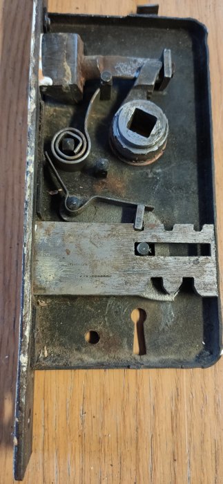 Öppet gammalt lås inuti; fjädern, tumvred, skruvar, och plattor i metall på träbotten.