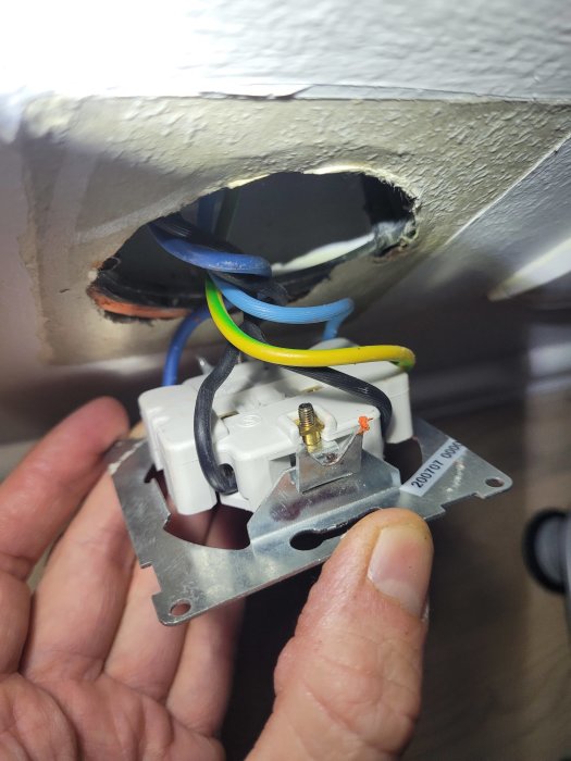 Installation av strömbrytare med exponerade elektriska kablar i en vägg. Hand syns hålla brytaren.
