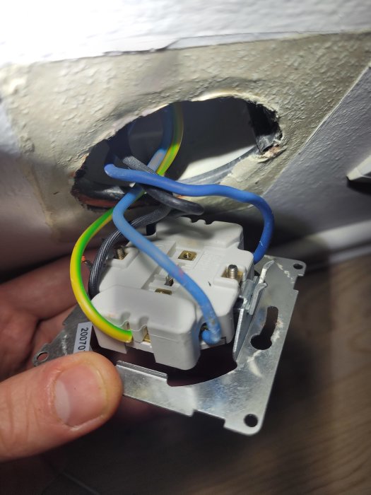Eluttag monterat i öppen vägg, exponerade elledningar, oavslutat elinstallationsarbete, hand håller komponent.