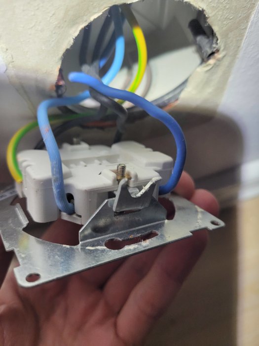 Öppen eluttaginstallation, osäkert, oskyddade kablar, blå neutral tråd, ej färdigställd, hand i bild.