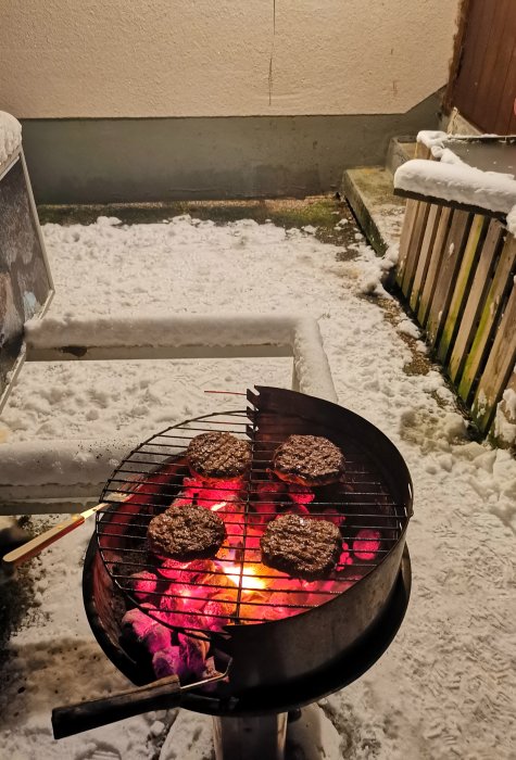 Grillning av hamburgare på kolgrill utomhus i snöigt landskap på natten.