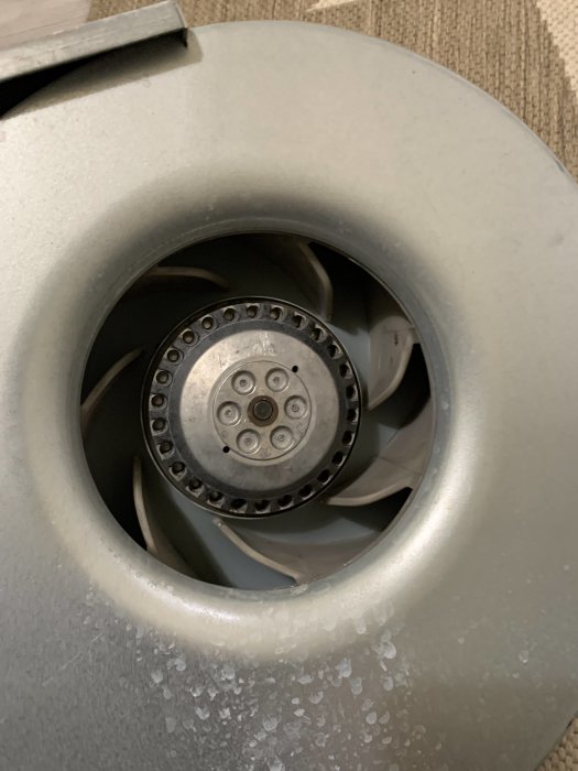 Grå fläktblad i ett ventilationssystem med synliga dammpartiklar och slitage.
