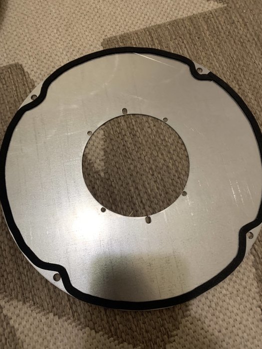 Cirkulär metallskiva med hål och fästpunkter på texturväv. Troligen en maskindel eller komponent.