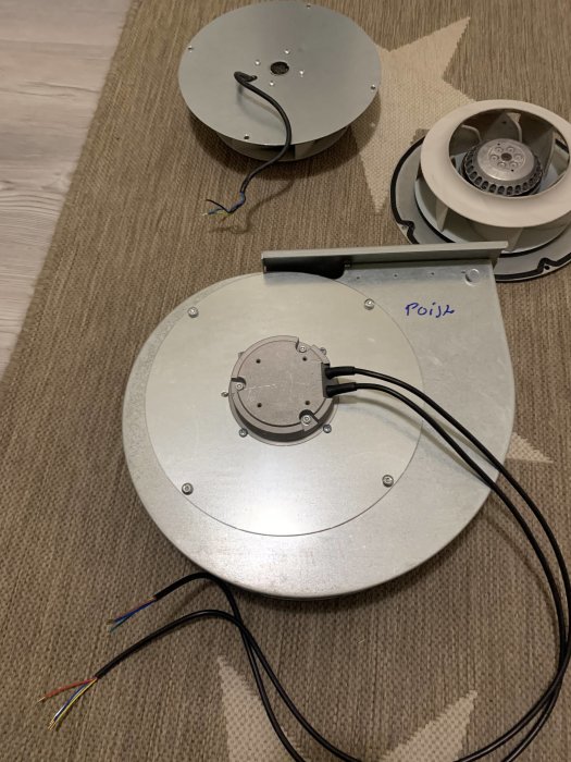 Demonterad taklampa med elektriska kablar, hus i metall, ligger på ett golv med matta.