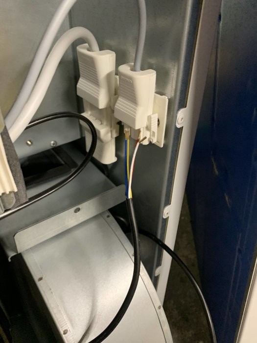 Eluttag med kopplade kablar, exponerade ledningar, nära metallskåp, installationsmiljö.