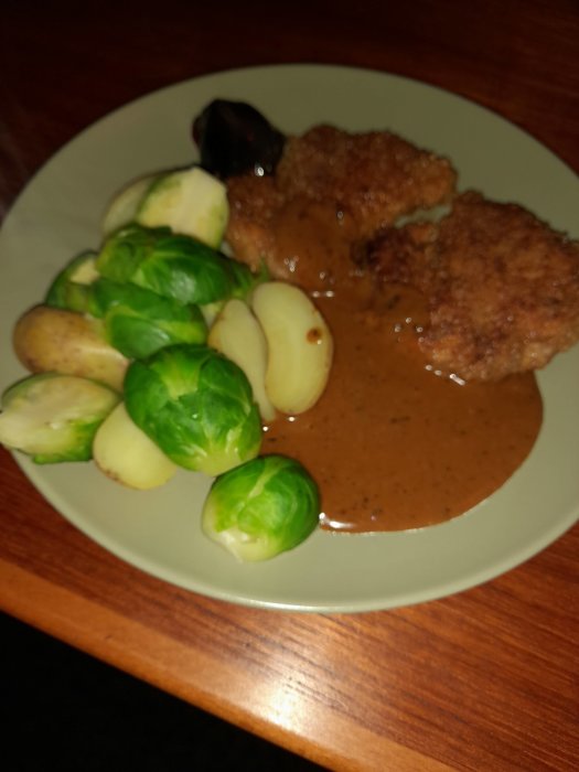 En tallrik med panerad schnitzel, sås, brysselkål och potatis, suddig bakgrund.