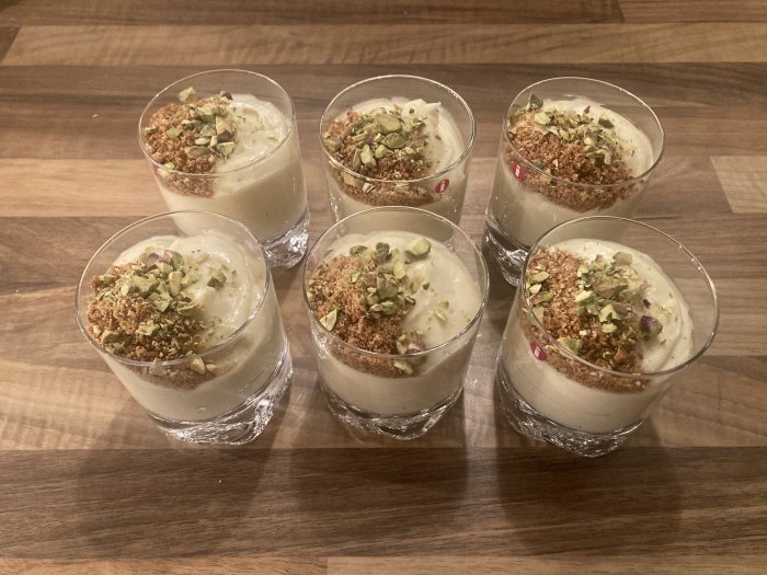 Glas med efterrätter, grädde och finfördelade nötter, träbakgrund, hemgjord presentation, dessertbuffé.