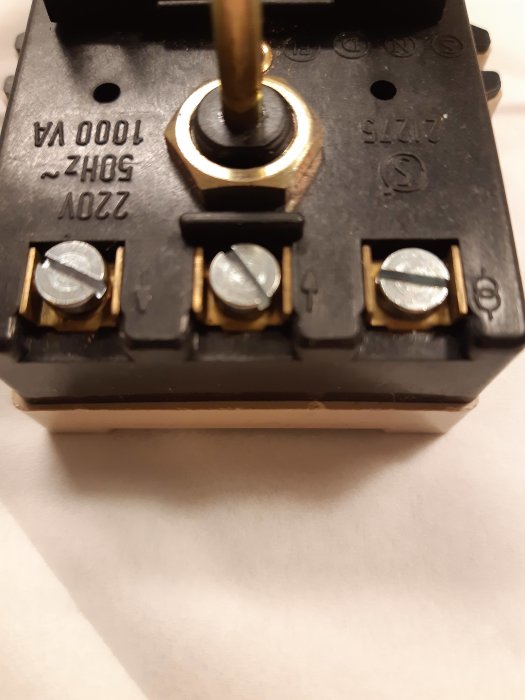 En elektrisk komponent med terminaler, skruvar, och ansluten gul kabel. Teknisk, oskarp förgrund, vit bakgrund.