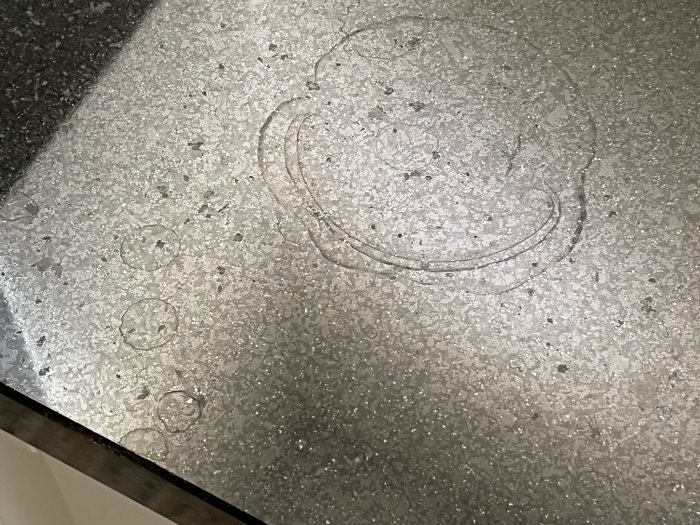 Grå texturerad yta med vattenringar och droppar, speglar kanske nyligen avställt glas eller hällning.