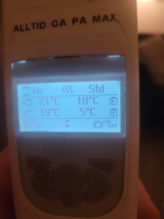 Digital termostat visar temperaturinställningar, text "ALLTID GA PA MAX" överst, oklar omgivning i bakgrunden.
