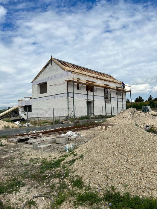 Ett oavslutat hus under konstruktion med byggnadsställningar och byggmaterial synligt. Molnig himmel ovanför.