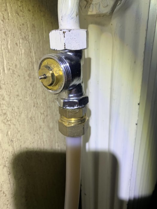 Ett vattenrör med avstängningsventil och ansluten slang nära en radiator, med vitmålade ytor bakom.