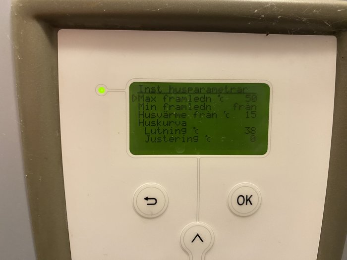 Digital kontrollpanel med grön display som visar värmeinställningar. Tre knappar under. Spindelväv i hörnet.