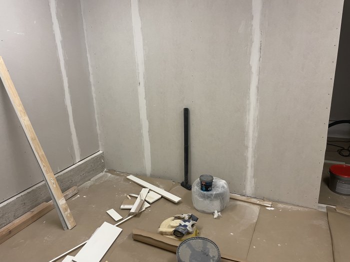 Omfattande renovering, oavslutad gipsvägg, spackelarbeten, byggmaterial och verktyg på golv.