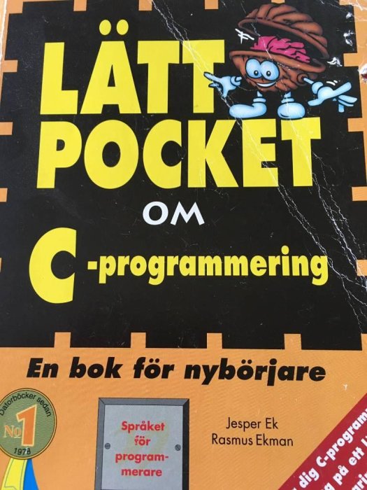 Svensk bok om C-programmering för nybörjare med tecknad figur på omslaget, slitna hörn, gul och svart design.