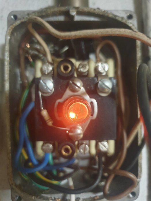 Elektrisk apparat med kretskort, anslutna trådar, och en lysande röd lampa inuti en metallram.