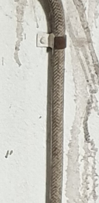Ett fäste håller fast en elkabel på en sliten vit vägg.