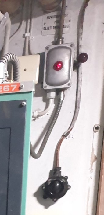 Industriell kontrollpanel med röd indikatorlampa, strömbrytare och ledningar på en vägg.