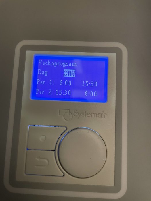 Digital timer för ventilation med programmerade tider, blå bakgrundsbelysning, väggmonterad, knappar och varumärke synligt.