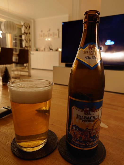 Ölflaska och glas på bord i mysigt vardagsrum, skumkrona, avslappnad atmosfär.
