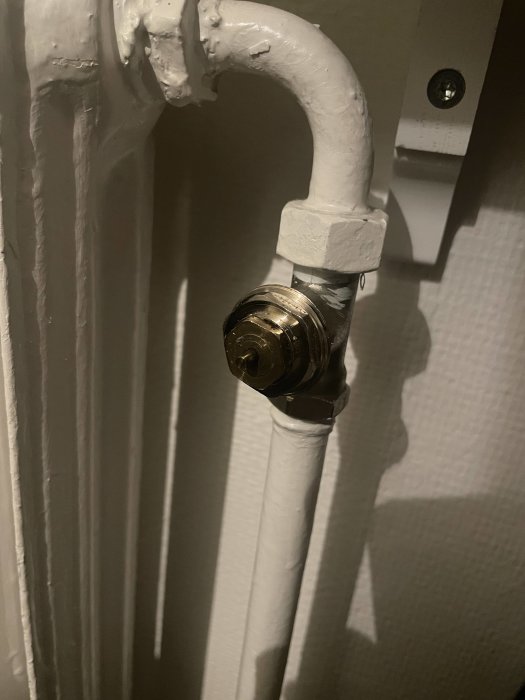Vitmålad, vertikal radiator med en termostatventil och rör, mot en tapetserad vägg.