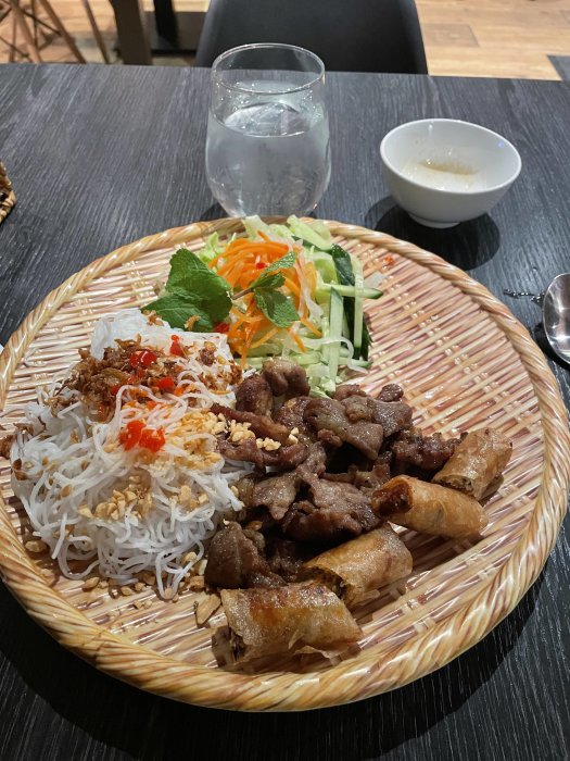 Vietnamesisk mat med nudlar, grillat kött, färska örter, vårrulle, grönsaker, jordnötter, chili, och fisksås. Glas med isvatten.