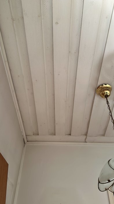 Vit trätakpanel, guldig taklampa, del av vägg och lampa.