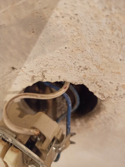 Öppen eluttaget utan täckplatta, synliga eltrådar, betongvägg, potent risk för elolyckor.