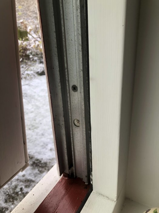 Ett fönster öppet mot ett snötäckt landskap; träram; metallspår; skruvar; närbild; inomhusperspektiv.