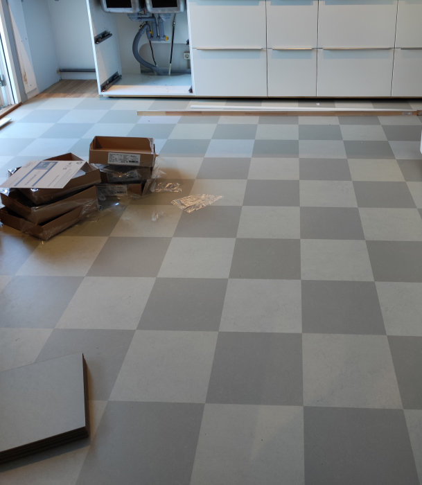 Tomrum, schackrutigt golv, vita skåp, renovering, kartonger och byggmaterial, osammanhängande delar på golvet.