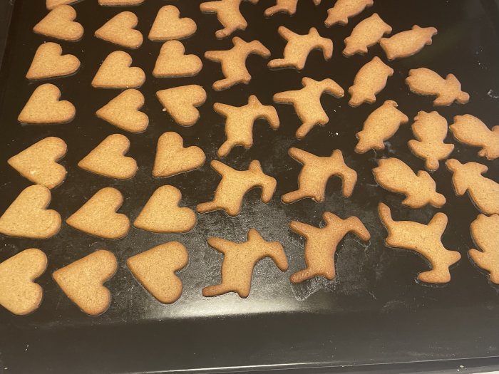 Nybakade pepparkakor i form av hjärtan och djur på en plåt.