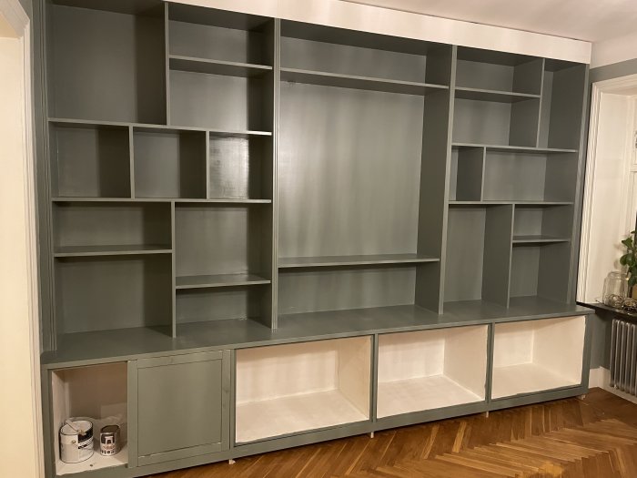 Stor tom grå bokhylla i ett rum med trägolv och målarburk bredvid.