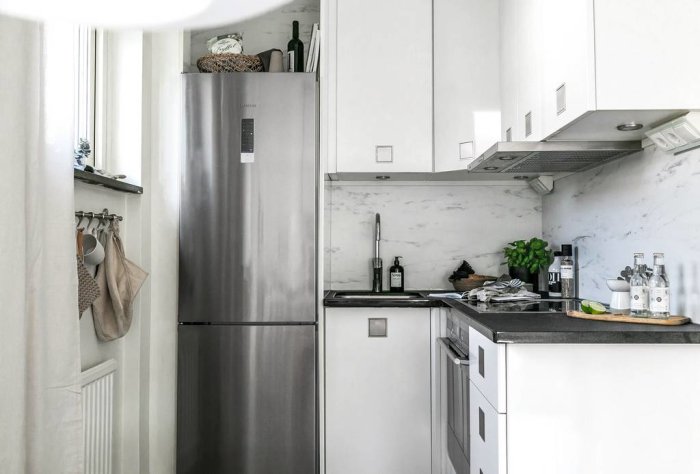 Modernt kök, rostfritt kylskåp, vita skåp, marmormönstrad stänkskydd, diskbänk, fläkt, svart bänkskiva.