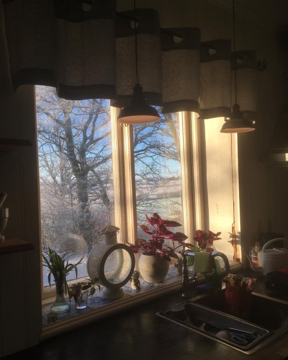 Kök med fönster, vinterlandskap utanför, julstjärna, lampor, diskbänk, mysig atmosfär, morgonsol.