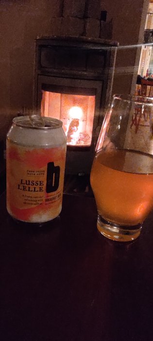 Ölburk och glas framför öppen spis. Mysig stämning. "Lusse Lelle" på burken antyder säsongsmässig dryck.