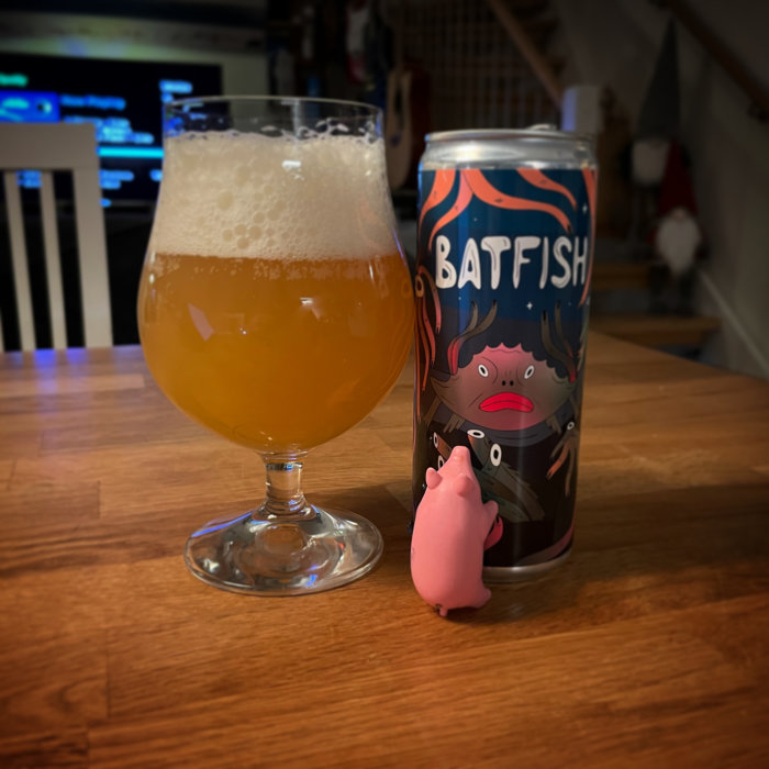 Ölglas med skum, burk med "Batfish"-design, rosa figur, inomhusmiljö, träbord, bostadsbakgrunden oskarp.
