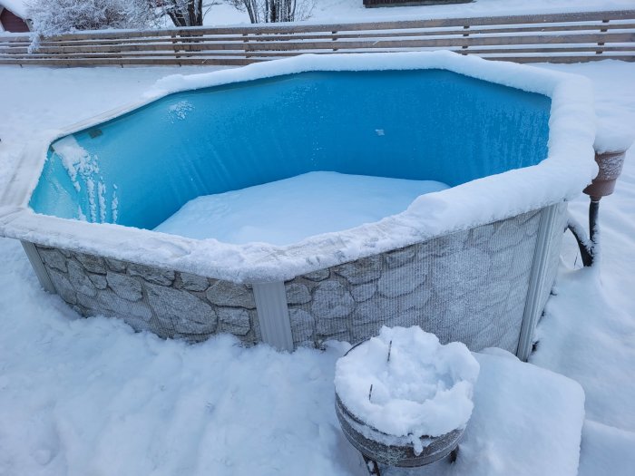 Utomhuspool täckt med snö under vintern, omgiven av snöig mark.