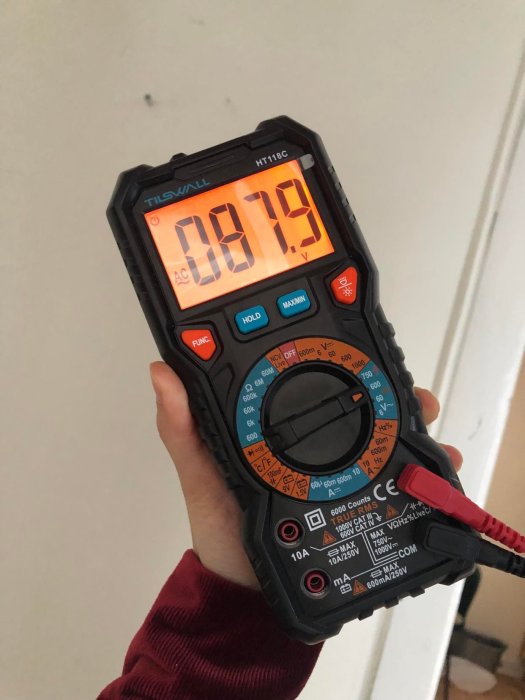 Hand håller en digital multimeter som visar 081.9V på displayen.