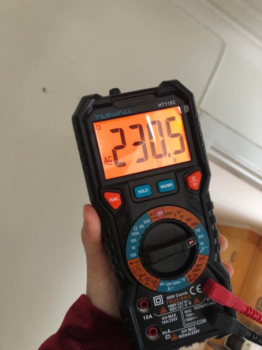 En person håller en digital multimeter visande 230,5 V, möjligtvis mätning av spänning i ett hem.