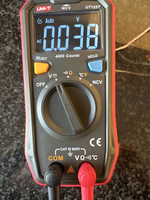 Digital multimeter visar växelspänning på 0.038 volt, med svart och röd sond ansluten, på granityta.