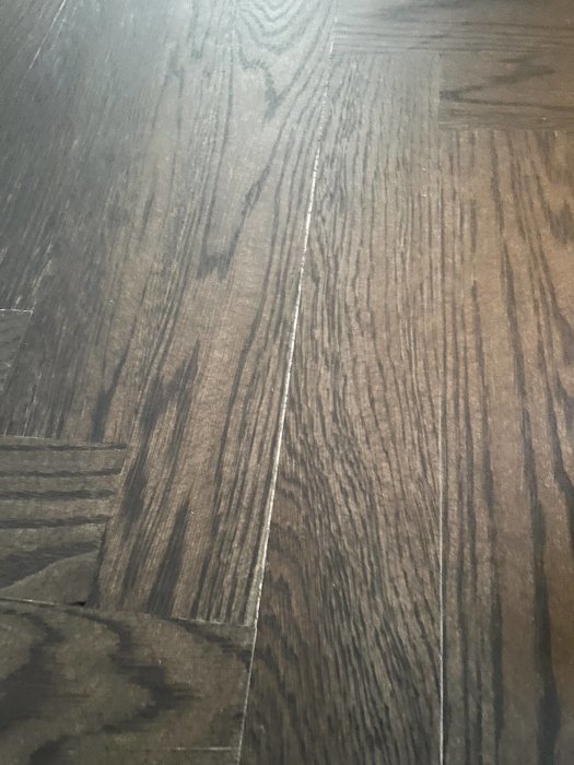 Mörkt trägolv; tydliga plankor och ådring; inomhusbelysning; närbild.