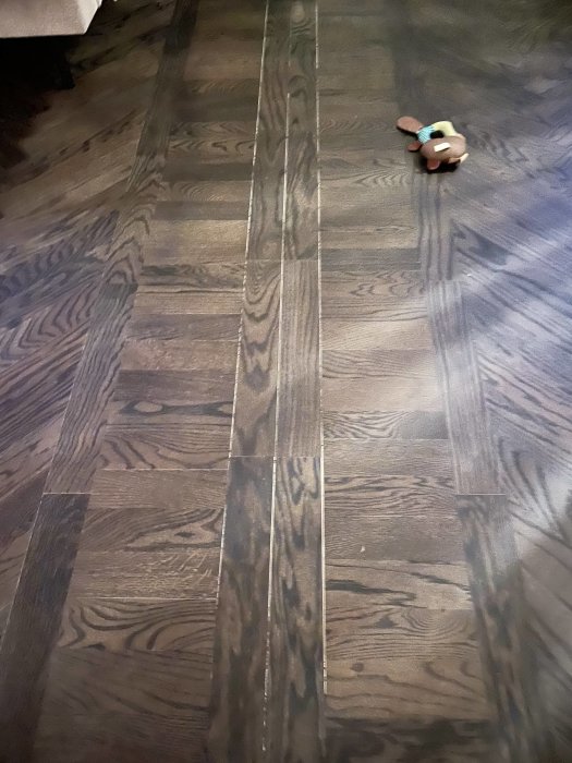 Mörkt trägolv med en liten leksaksfigur, delvis skuggigt rum, inomhus.