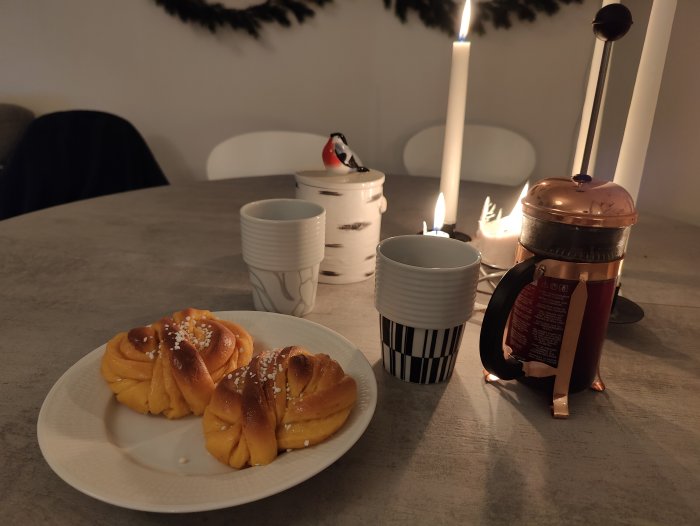 Mysigt fikastund med ljus, bullar, kaffe i presskanna och två koppar.