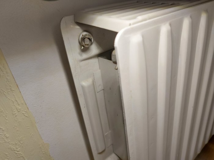 Väggmonterad radiator med termostat, närbild, inomhus, detaljvy av upphängning och värmeelement.