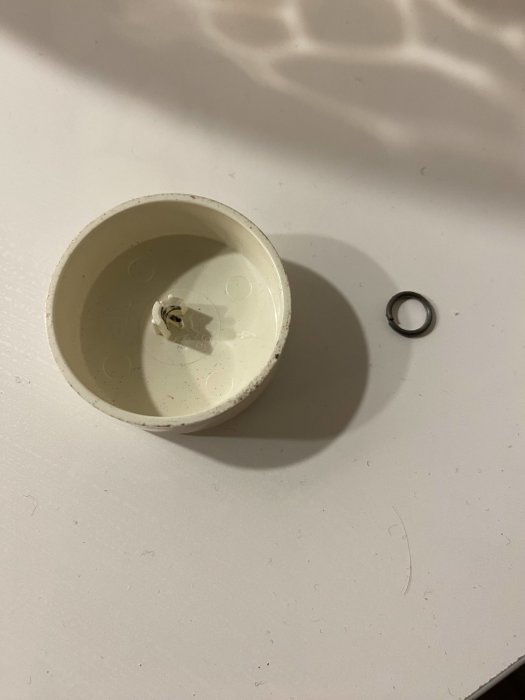 En genombränd glödlampa och en liten metallring på en vit yta.