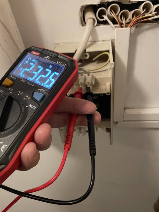 Multimeter används för att mäta spänning i en el-central, verktyg och öppen ledningsdragning syns.